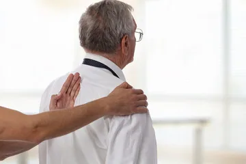 Healthcare provider performing manual examination or adjustment on patient's shoulder and upper back