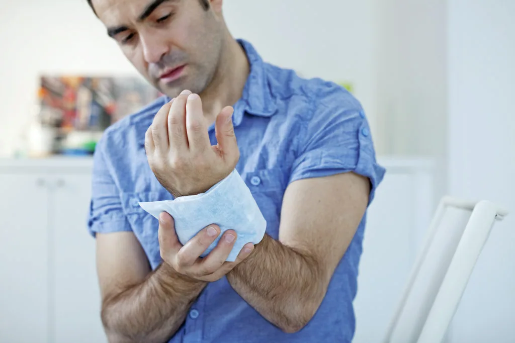 Man in blue shirt examining his injured hand wrapped in white bandage