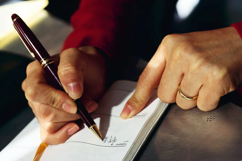 Person signing a document with a dark red pen while wearing a gold ring