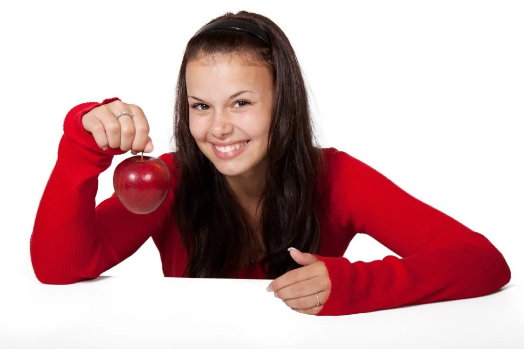 Woman in red sweater holding red apple while smiling at camera