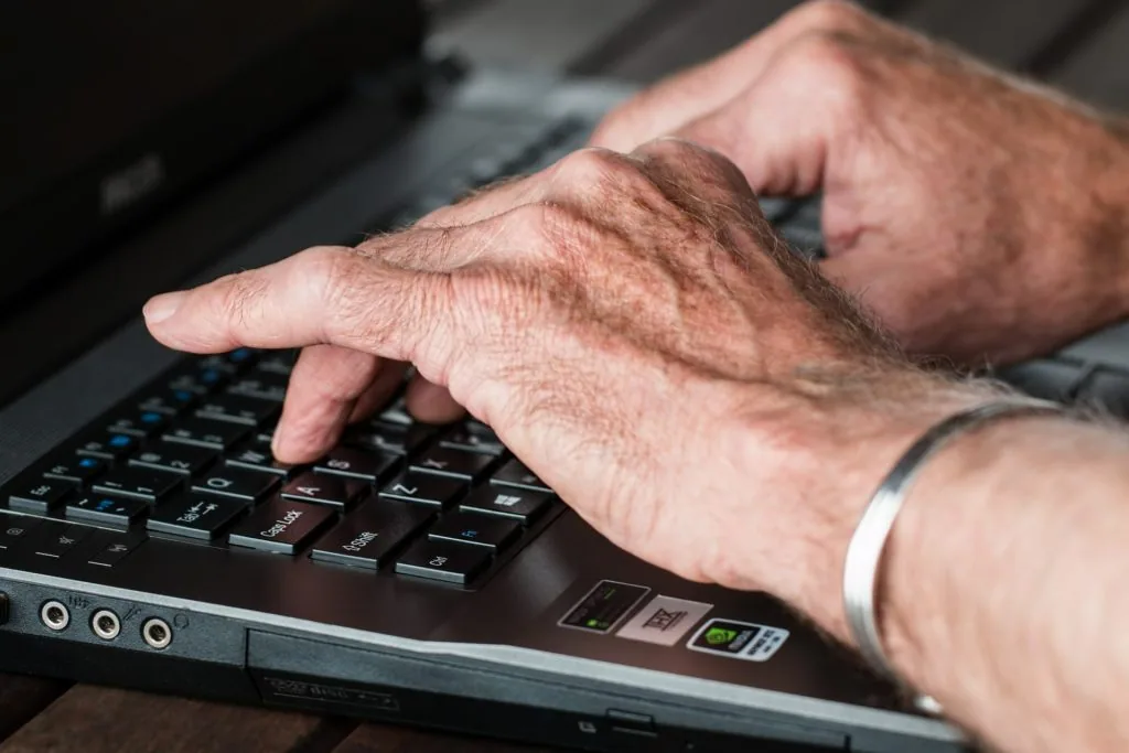 Older adult hands typing on a laptop keyboard